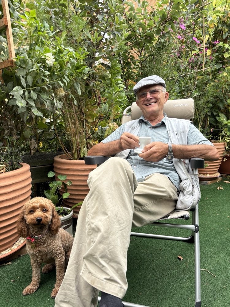 Sokol in a garden chair with a coffee, his dog Nala beside him, the garden all around.